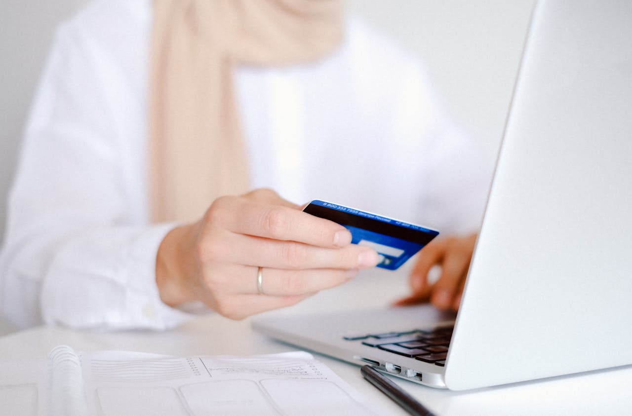 Person holding a credit card beside a laptop